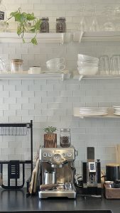kitchen counter with espresso machine on counter and white open shelving with minimalistic dishes on white subway tile