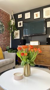 bright red tulips in a gold vase on a white coffee table in the living room of an apartment with exposed red brick walls