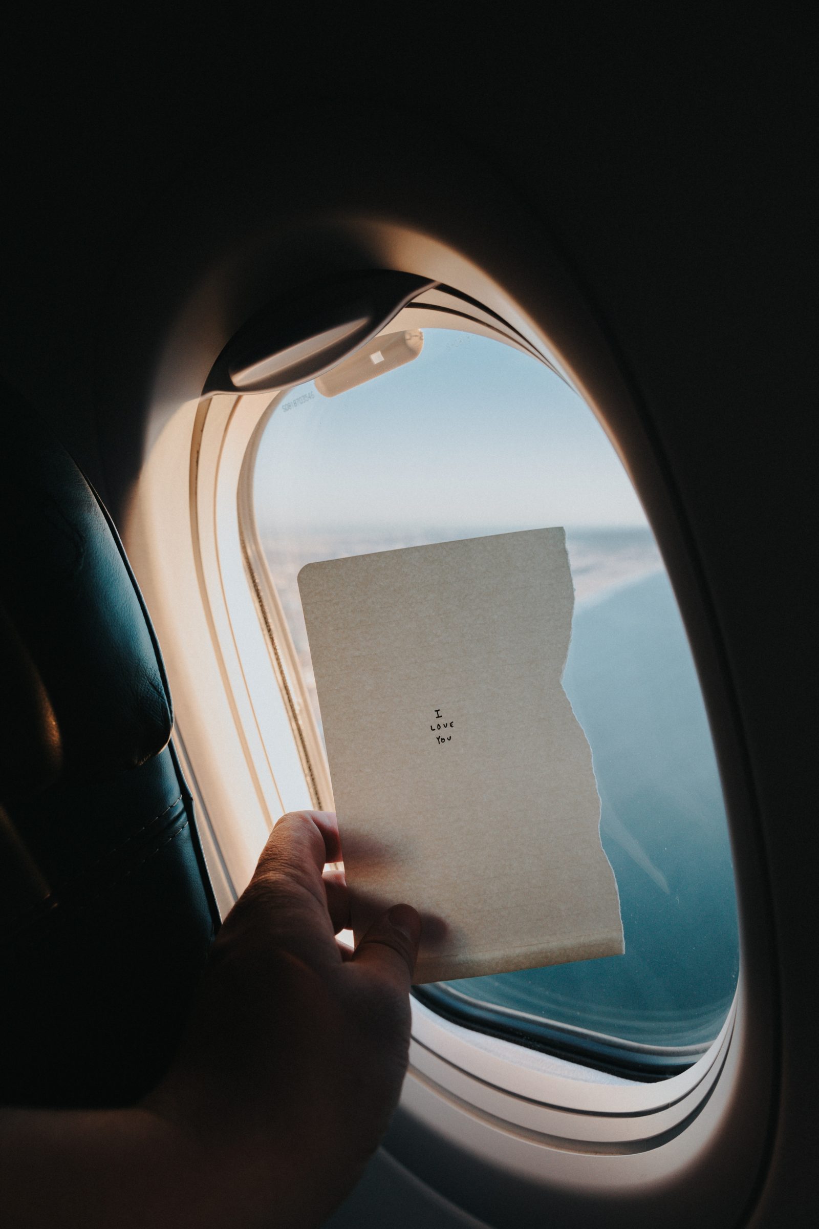 Woman by an airplane window holding up a peice of paper